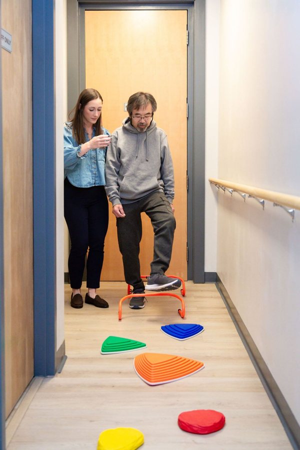 A patient practising balance steps along a hallway with her therapist