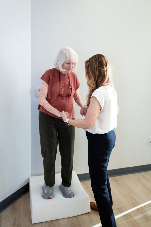 A therapist steadying a patient standing on a foam pad
